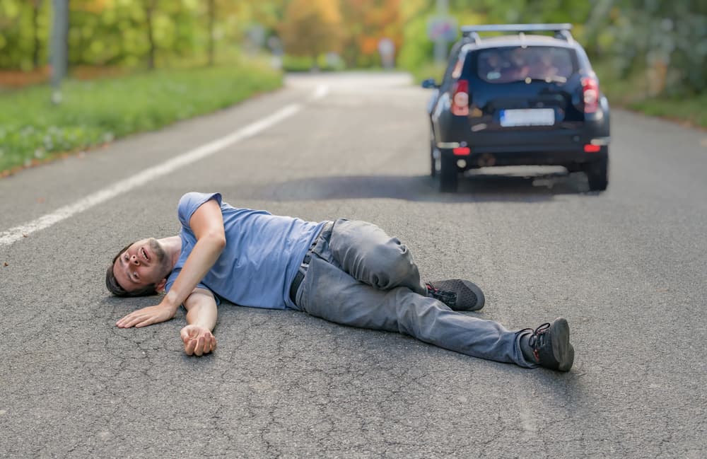 Hit-and-run incident: An injured man lies on the road in front of a car.