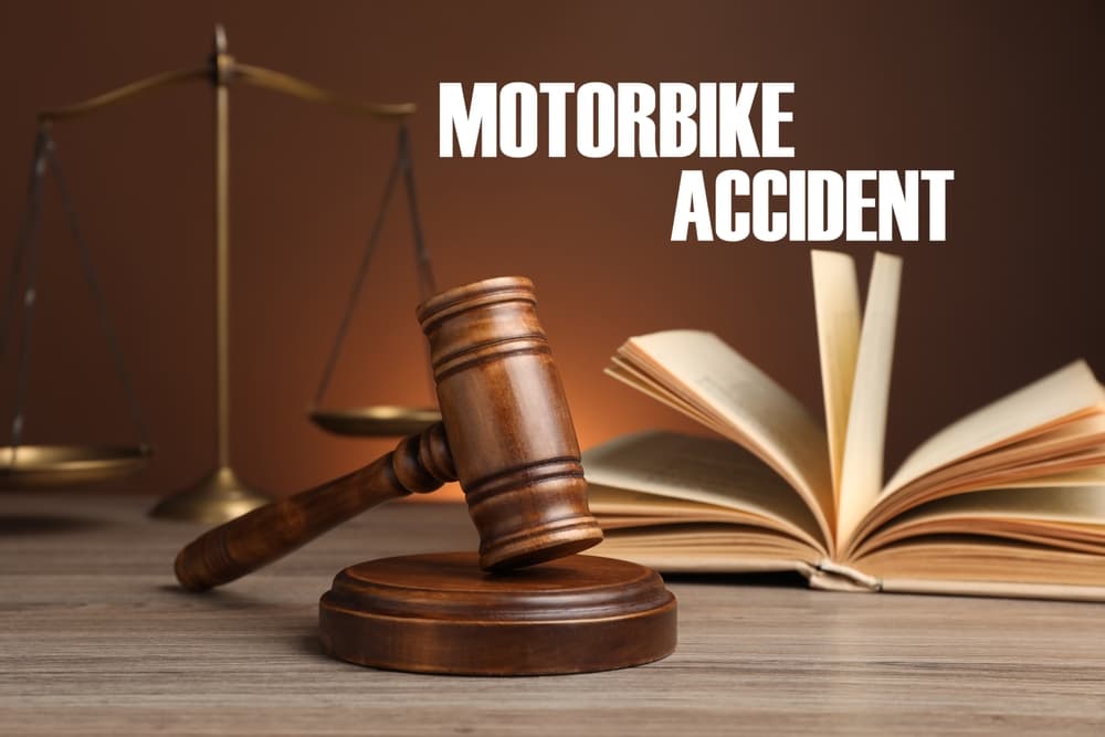 Motorcycle accident law concept: judge's gavel, scales of justice, and a legal book displayed on a wooden table against a brown backdrop.