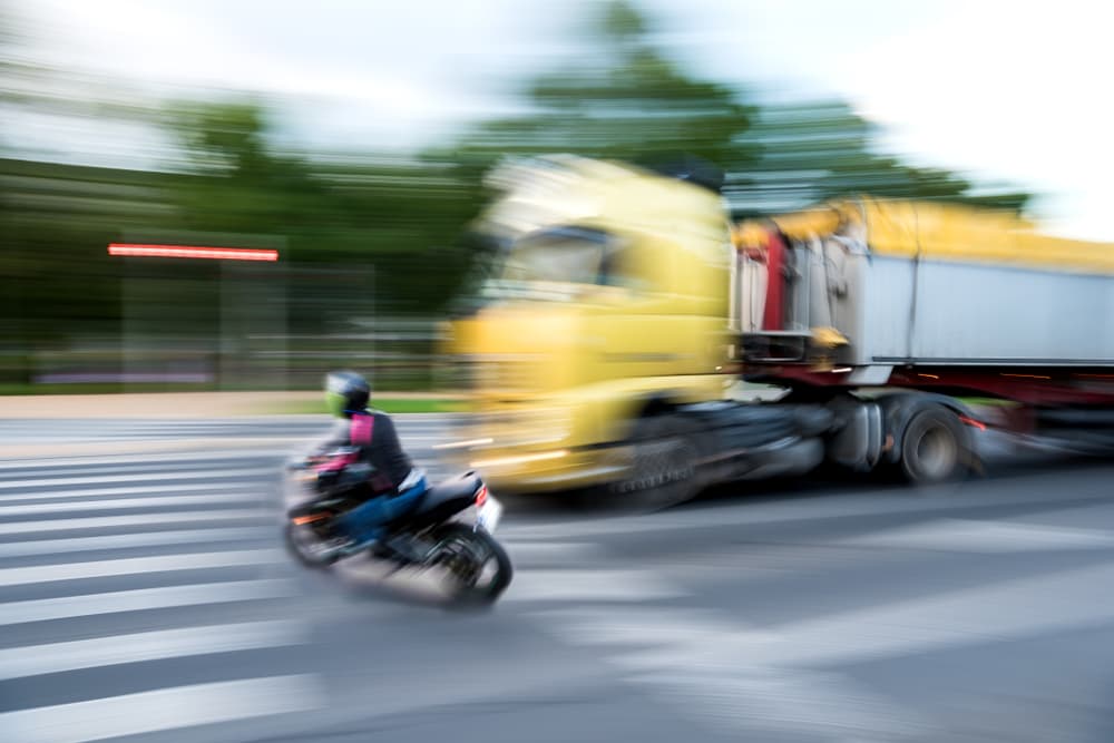 City traffic scene featuring a motorcyclist and a truck in motion, creating a sense of urgency and potential danger.