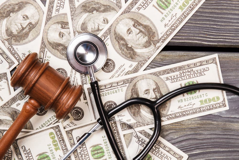 The concept of justice in medical corruption: a wooden gavel alongside a stethoscope and a stack of dollar bills.