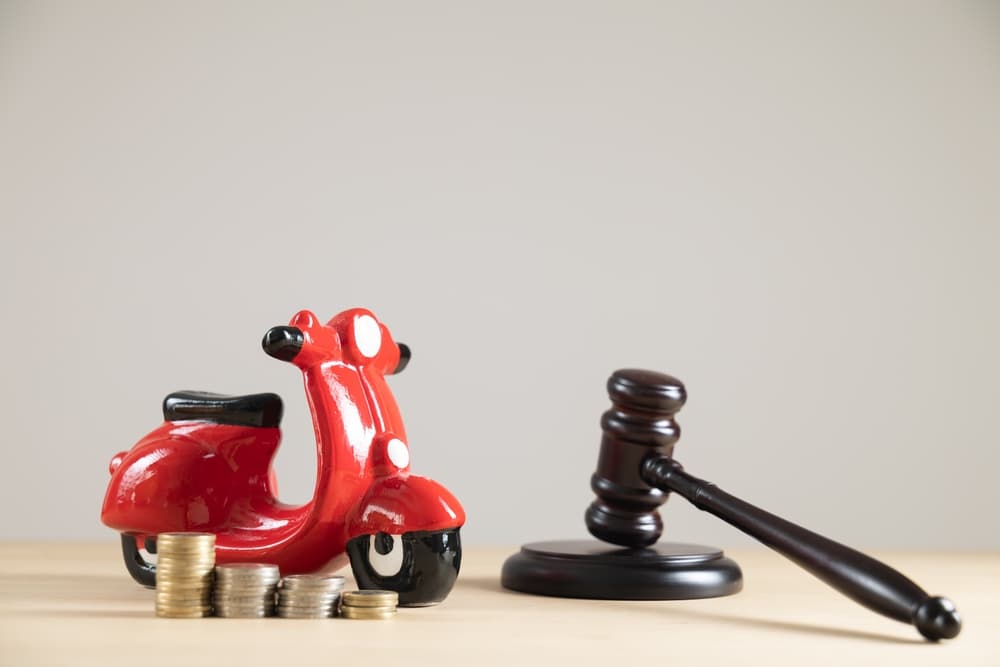 Close-up of a red motorbike piggy bank, judge's gavel, and cash on a plain background. 